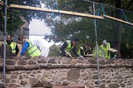 Five students in high-visibility jackets helping to re-plaster a wall.
